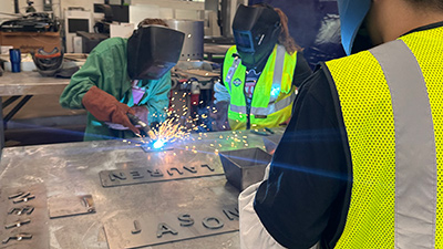 Workers in safety vest welding and fabricating sheet metal in a workshop